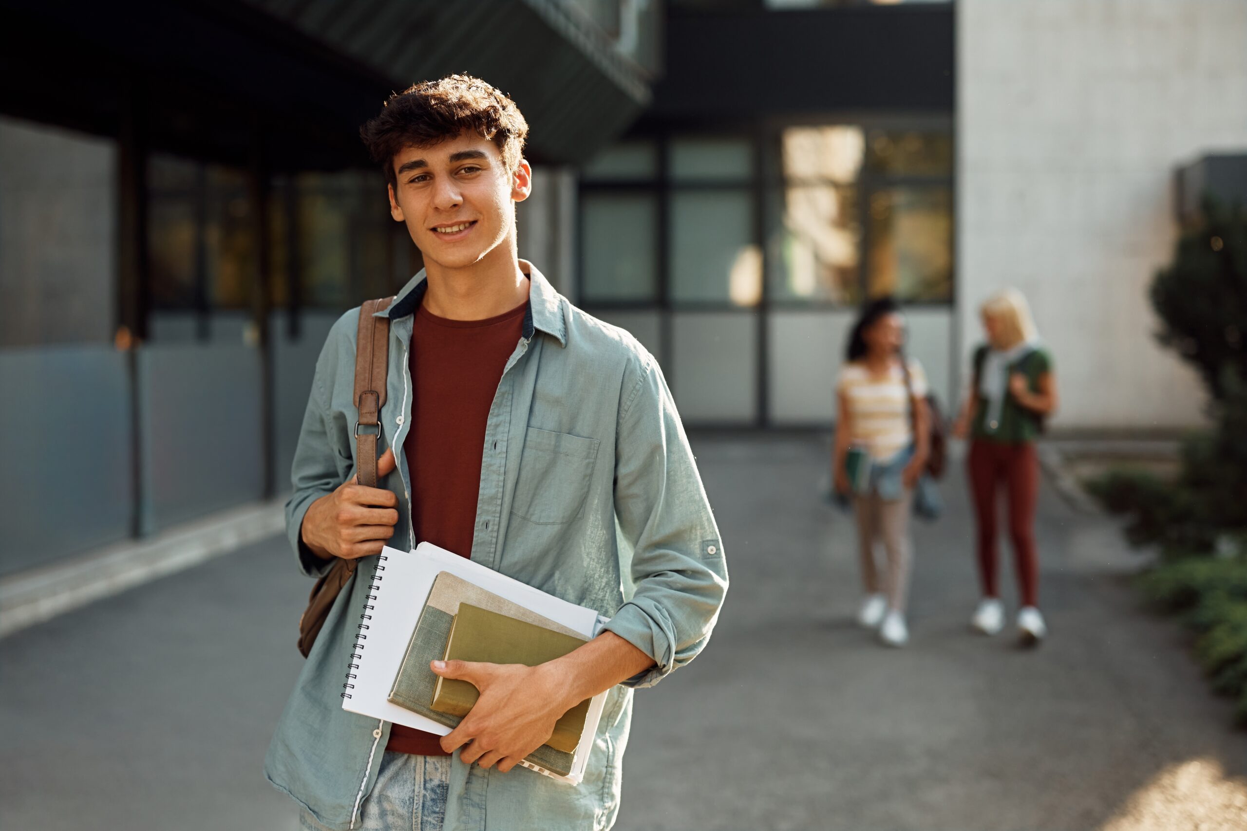 Young,Student,In,Front,Of,University,Building,Looking,At,Camera.